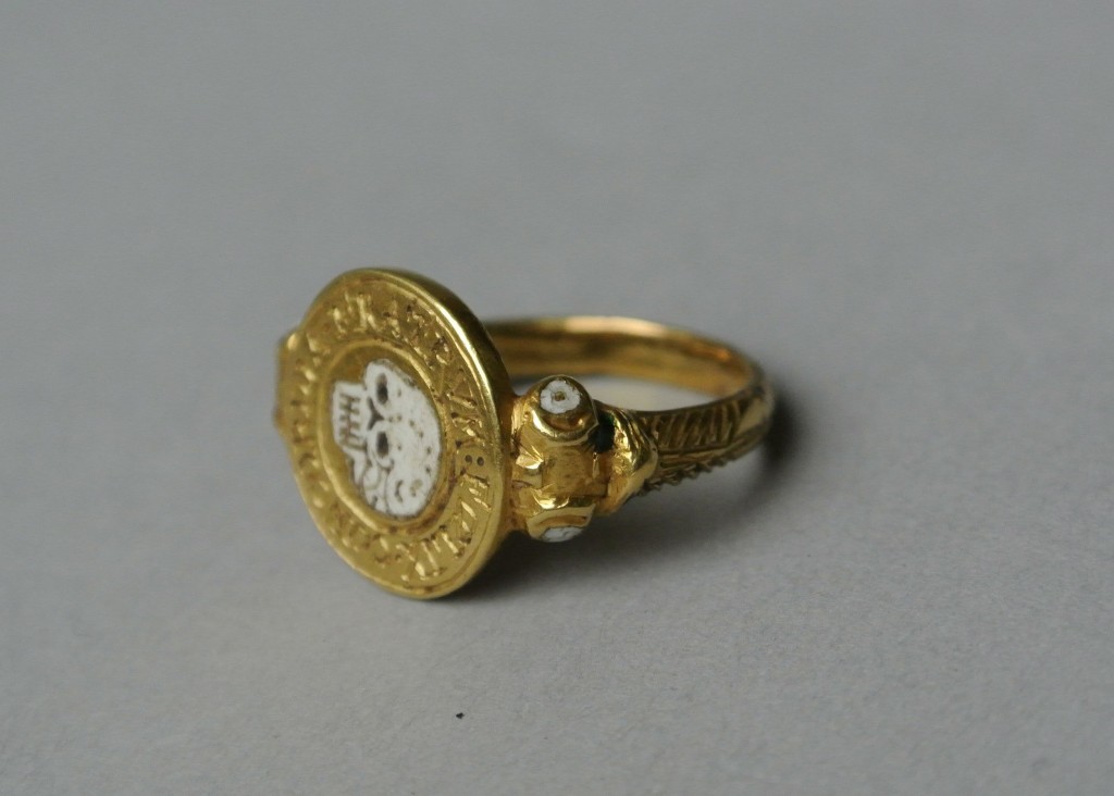 Mourning-ring; gold, with circular bezel containing enamelled skull (death's head) surrounded by the Latin legend: FOELIX CONCORDIA FRATRUM. The shoulders of the hoop are scrolled and ornamented with white and green enamel. At the back of the bezel are three engraved letters, H, above I and A. No maker's mark.