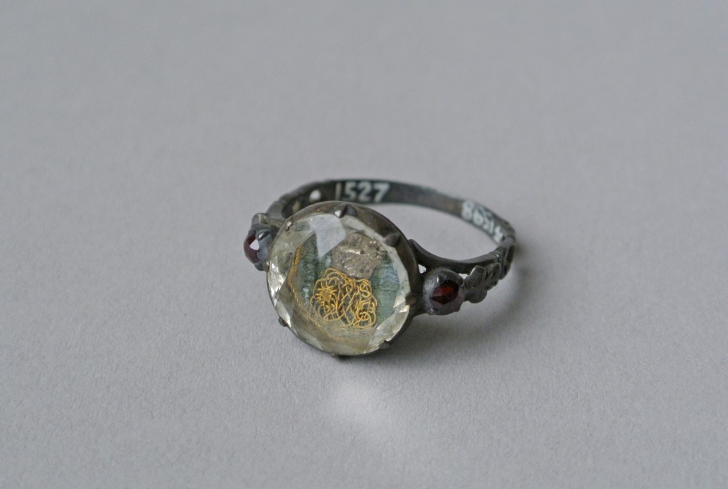 Mourning ring; silver; oval bezel reeded beneath and containing cipher in gold thread with basket in silver on a green fabric background, beneath rock crystal (or glass); each shoulder set with garnet and pierced with scrolls.Probably originally gilded. No maker's mark.