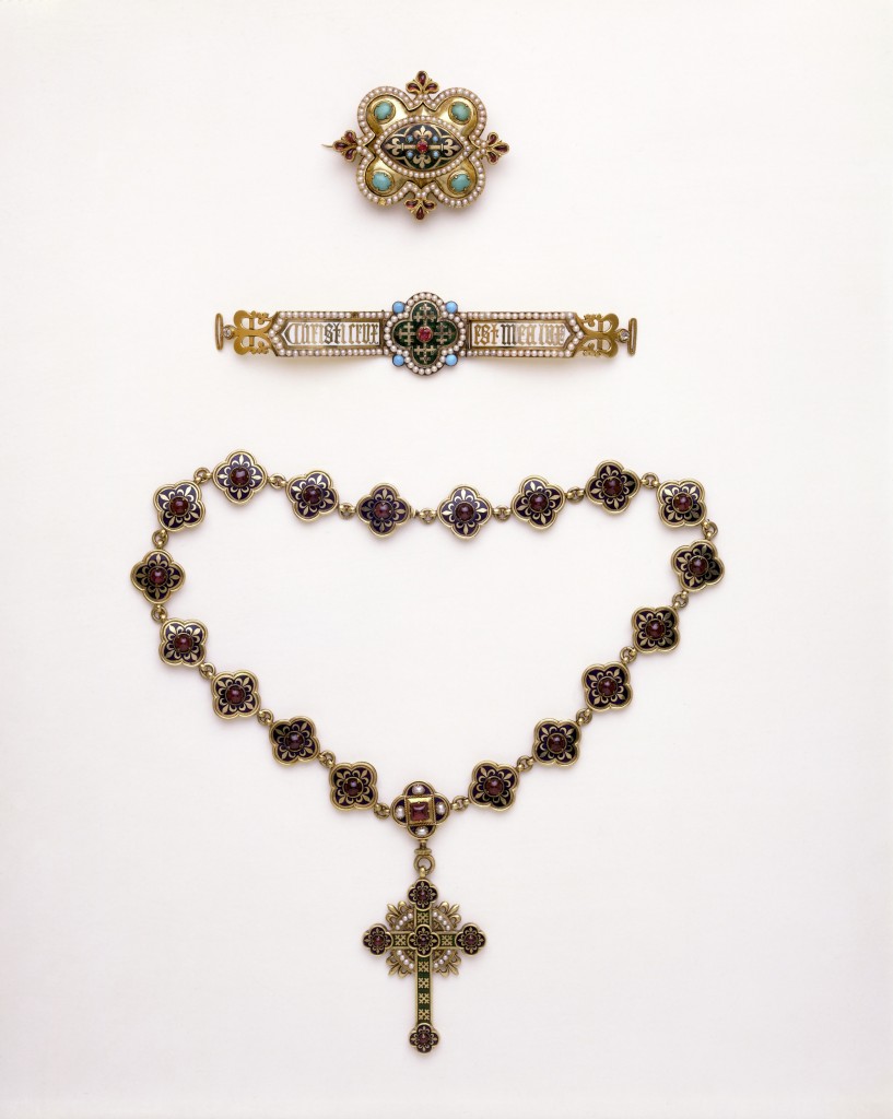 Object Type  The necklace is composed of 19 enamelled quatrefoils set with garnets. The pendant cross has quatrefoil ends decorated in the same manner as the links of the necklace. In each of the angles between the arms are four small pearls surmounted by a gold fleur-de-lis.  People  The necklace and pendant were made for Louisa Burton, the second wife of the architect A. W. N. Pugin (1812-1852). Pugin's account with John Hardman & Co. of Birmingham contains an entry on 21 December 1843 for 'A Gold enamel Chain & Cross' costing £47. 15s. Louisa died eight months later.  The cross and chain became part of the large parure (set) of jewellery prepared by Pugin for his intended third bride, Helen Lumsdaine. He persuaded Helen to convert to Catholicism, but in 1848, before they could be married, he was parted from her at the insistence of her relatives. Pugin subsequently married a Catholic, Jane Knill, on 10 August 1848. The society gossip Ralph Nevill recalled her as a very pretty woman, her every jewel mounted 'in a Gothic setting'. The set was exhibited in Pugin's Medieval Court at the Great Exhibition of 1851, where it was admired by Queen Victoria.