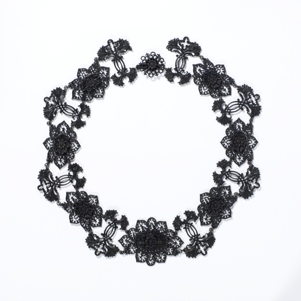Cast-iron jewellery was an inexpensive but fashionable novelty for consumers in Europe and America from around 1800 to 1860. Developed in Germany in 1806–7 and often worn during mourning, it became the symbol of Prussian patriotism and resistance to Napoleon I in the Prussian War of Liberation fought from 1813-15. Women donated gold jewellery to their country in exchange for iron inscribed ‘I gave gold for iron’.  The transformation of cast iron, a dark metal of little value, into a fashionable product was an important Prussian manufacturing success. Factories became adept at casting small, delicate parts which could be assembled to create the jewellery. A renewed interest in the Medieval past throughout Europe brought stylistic change. After 1815, the Neo-classical designs of earlier Berlin ironwork were replaced by Gothic motifs such as the trefoil, quatrefoil, and fine pointed arches. The jewellery quickly gained an international profile. Demand peaked in the 1830s, when Berlin alone had 27 foundries and manufacture spread to France and Austria.