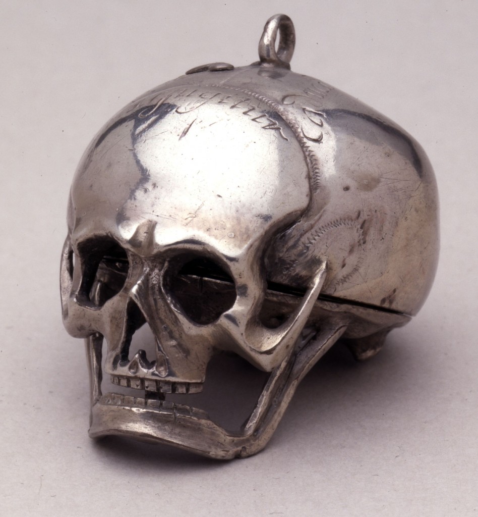 SILVER CASED VERGE WATCH IN THE FORM OF A HUMAN SKULL. . MOVEMENT FRAME: Full-plate with circular gilt-brass plates and four baluster pillars. : MAINSPRING & SET-UP: Gilt-brass barrel with tangent-screw set-up mounted on the potence-plate. : FUSEE & STOP-WORK: Gilt-brass fusee with chain and English stop-work. : TRAIN: Four wheel train, the contrate wheel solid. : ESCAPEMENT & BALANCE: Verge escapement, the crown wheel running between riveted potence and counter-potence. There have been extensive alterations to both potence and counter-potence suggesting that the crown wheel is most likely to be a replacement. Verge and steel 2-arm balance not original. The pierced and engraved gilt-brass foliate balance cock is also a replacement. There are a number of vacant holes,both threaded and plain, in the potence-plate where it appears that the original balance cock was replaced by a balance bridge and balance spring. : DIAL & HAND: An engraved border on the front of the pillar-plate surrounds the pinned-on silver dial which has Roman hours I-XII, arrow-head half-hour marks and a quarter circle. The blued-steel hand is a replacement. : CASE: Silver case in the form of a human skull, the lower plate, including the lower jaw being hinged at the back. On top there is a cover for the winding hole. Silver hanging loop. There are inscriptions in various places on the outside of the skull. Movement hinged to case at XII.