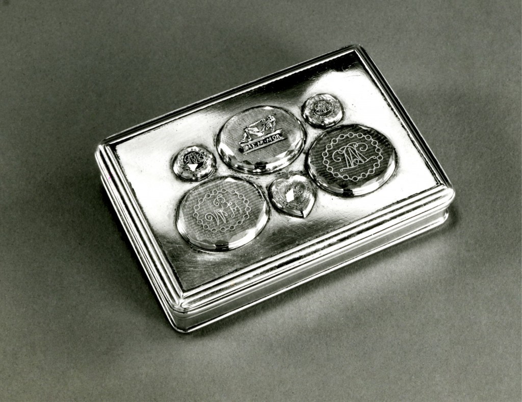 Silver box with mouldings on edge of lid and base with a gilt interior and a hinged lid: set with five memorial ovals and one in the form of a heart, on corded silk under faceted rock-crystal. One shows an enamelled skeleton with an inscription and the others consist of gold wire monograms.