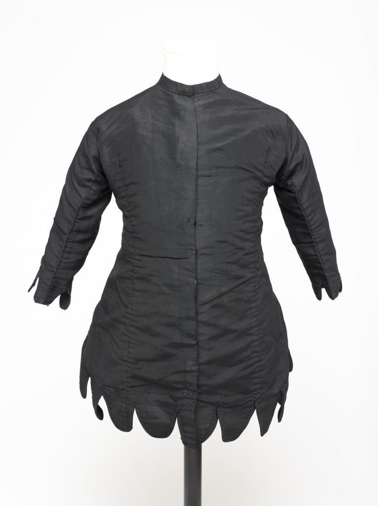 Little girl's mourning garment, in the form of a short princess-line coat dress made of black grosgrain lined throughout with white cotton. The garment has a rounded neck with a self fabric neckband, and fastens the length of the front with metal hooks and stitched loops. The hem and wrist-length sleeves are finished with vandyke tabs bound and faced with self fabric. The coat is shaped to fit at the waist: it is cut in six pieces, the front two of which have long darts. Lines of stitch holes indicate that two mitred pieces of fabric which were originally positioned at the waist back have been removed.