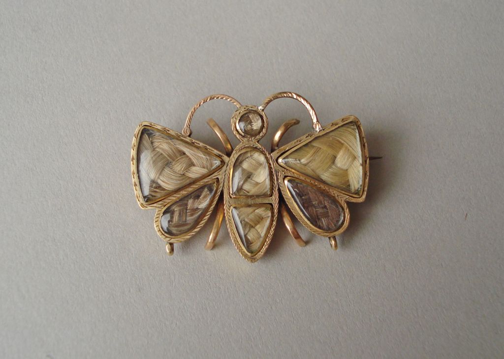 Gold brooch in the form of a butterfly, with seven plaited hair arrangements under glass, two for each wing and three for the body. The gold mounts with engraved decoration. The reverse inscribed with initials and the date 1839 and 1842.