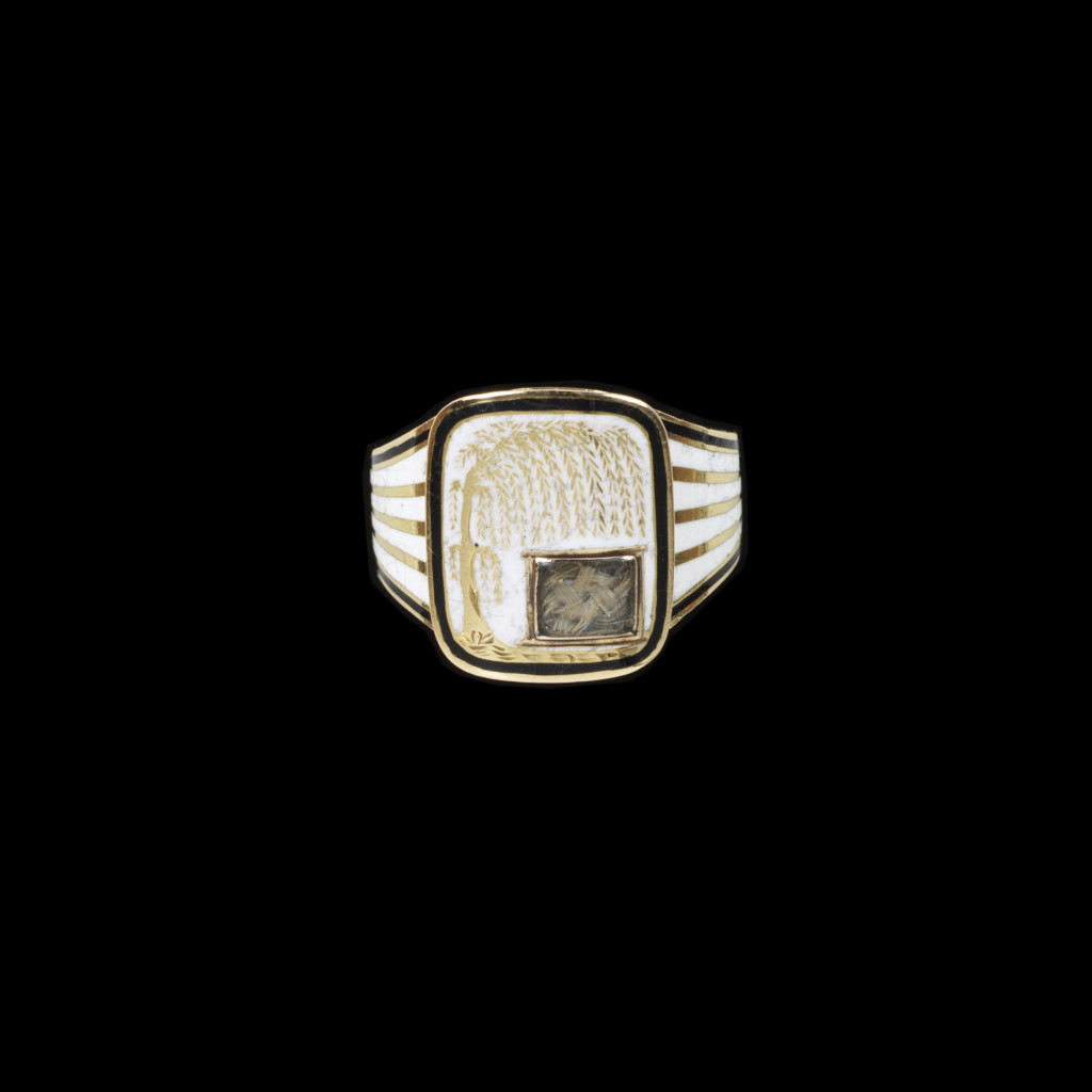 Gold mourning ring enamelled in black and white. The shaped rectangular bezel, with a willow tree reserved on white enamel with a small glazed locket containing hair. Inscribed behind Anna/ Seward./ Ob. 25 March, 1809.' Aet. 66.