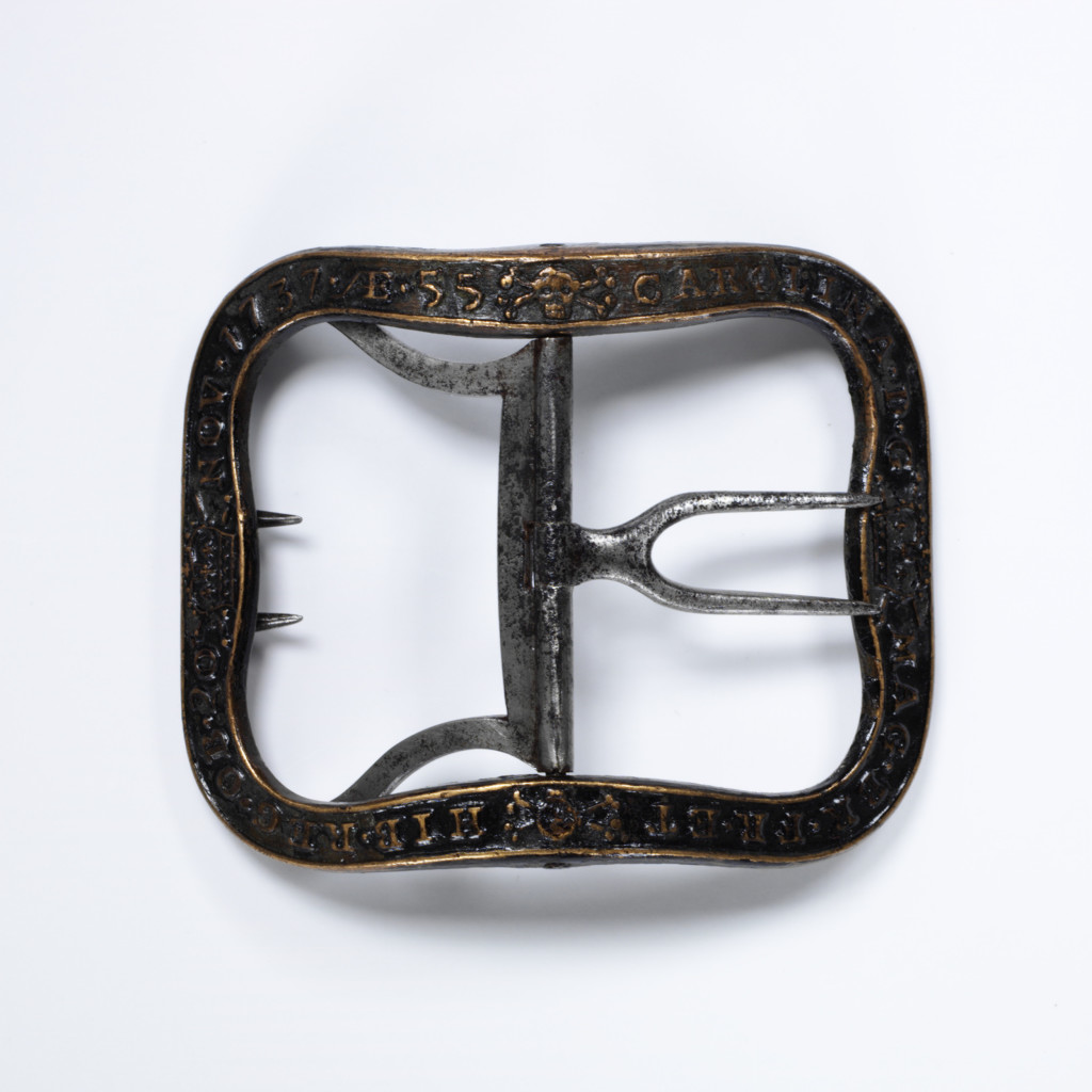 An inscription and symbols of mortality decorate the band of this black shoe buckle. The inscription tells us that it was made to commemorate the death of Queen Caroline, consort of George II, who died on 20 November 1737, in her 55th year.