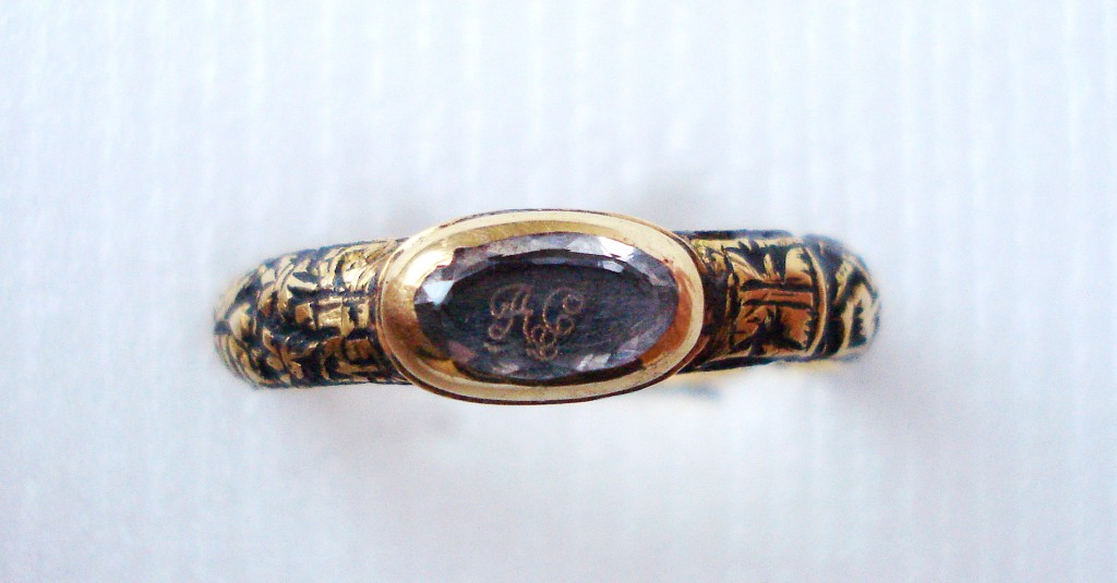 Mourning-ring; gold; oval bezel containing monogram in gold thread with letters under crystal; round hoop, reserved in metal on ground of black enamel, hour-glass, spade and pick crossed, cross-bones and skeleton; engraved inscription. No maker's mark.