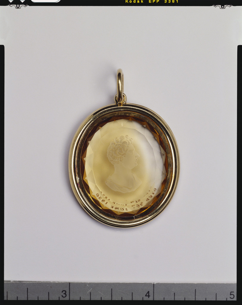 Oval faceted citrine cut in reverse intaglio with a bust of George IV (1762-1830) in profile to the left. The King is bare headed and wears classical drapery fastened by a brooch on his left shoulder. The front of the citrine is inscribed below the bust: DIED 26TH JUNE 1830.