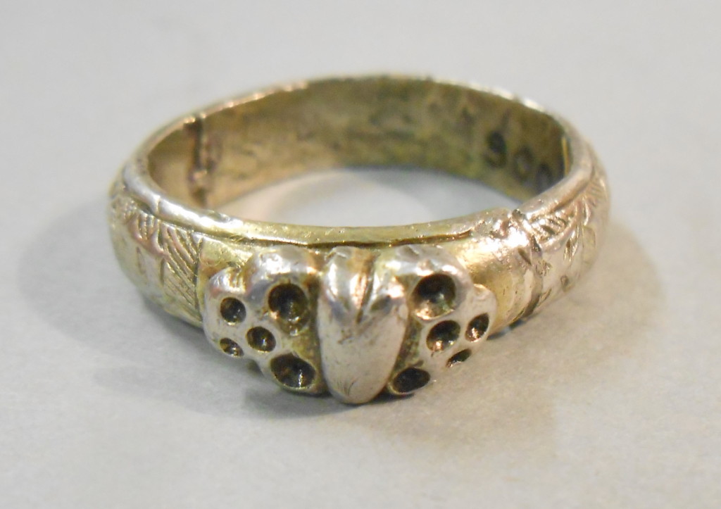 Silver gilt ring, the applied bezel with a heart between two death's heads. The hoop engraved with a worm and inscribed in black letter + iohes godefroy