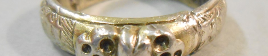 Silver gilt ring, the applied bezel with a heart between two death's heads. The hoop engraved with a worm and inscribed in black letter + iohes godefroy