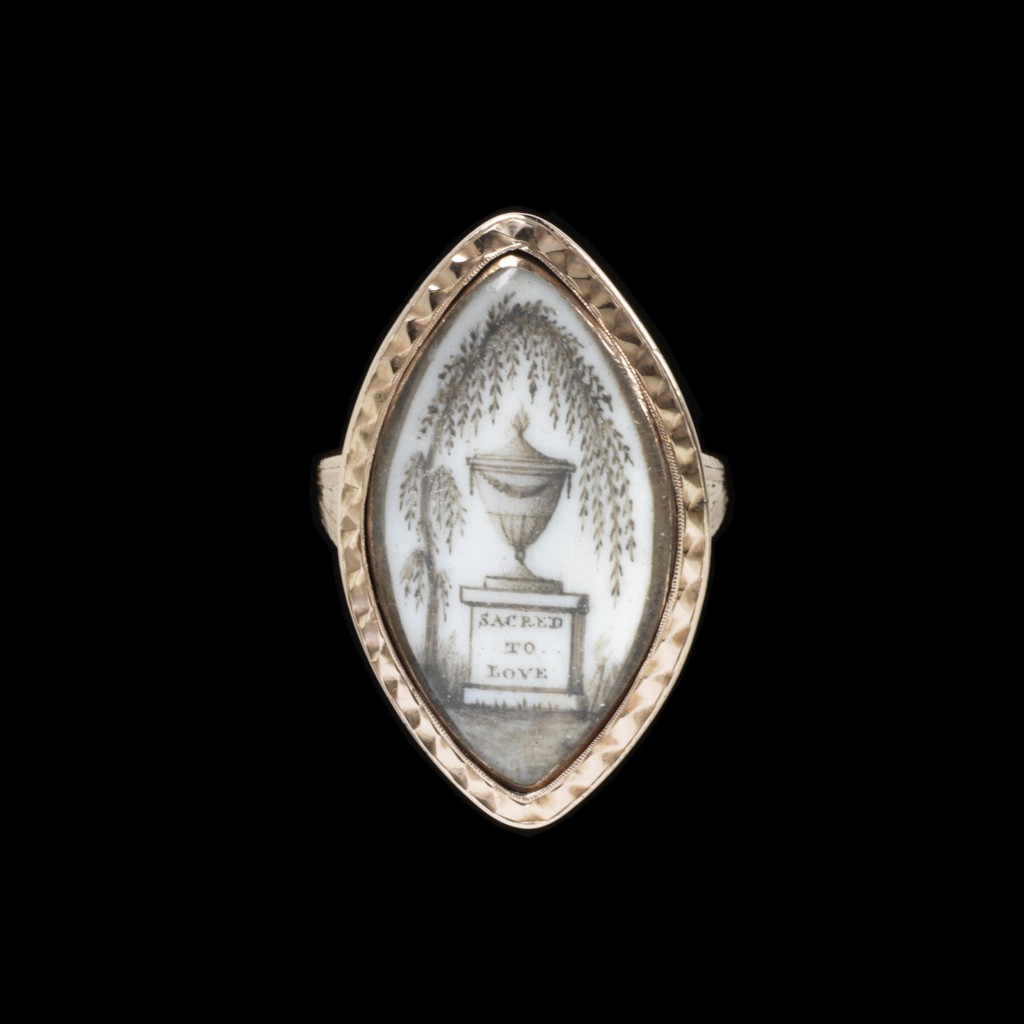 Gold mourning ring with a marquise bezel with a miniature of a weeping willow and an urn on a pedestal inscribed SACRED TO LOVE and behind with Ino. Amey Ob 18 Mar 1791 Aet 64.. The miniature is made from finely chopped human hair in a brown pigment painted onto ivory. Image courtesy of the V&A Museum.