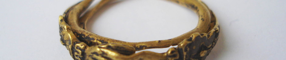 A gold fede and gimmel ring consisting of two interlocking and twisted hoops with clasped hands forming the bezel. Within the lower hand is a heart and, when the two hoops are joined, the top hand clasps this heart. The hands extend to the shoulders, becoming cuffs and these are decorated and partly enamelled. On the inside of each hoop is an inscription that remains concealed when the two hoops are shut.
