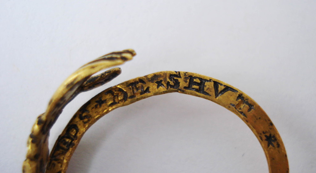 A gold fede and gimmel ring consisting of two interlocking and twisted hoops with clasped hands forming the bezel. Within the lower hand is a heart and, when the two hoops are joined, the top hand clasps this heart. The hands extend to the shoulders, becoming cuffs and these are decorated and partly enamelled. On the inside of each hoop is an inscription that remains concealed when the two hoops are shut.