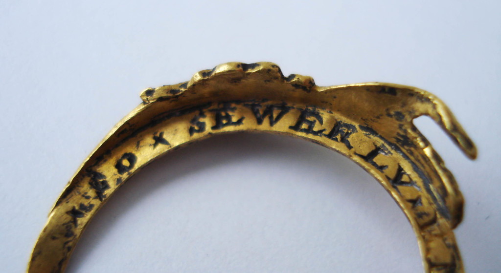 A gold fede and gimmel ring consisting of two interlocking and twisted hoops with clasped hands forming the bezel. Within the lower hand is a heart and, when the two hoops are joined, the top hand clasps this heart. The hands extend to the shoulders, becoming cuffs and these are decorated and partly enamelled. On the inside of each hoop is an inscription that remains concealed when the two hoops are shut.