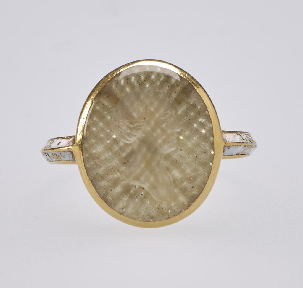 Small gold mourning ring, the centre set with oval crystal containing woven hair and carved with intaglio profile head of Princess Elizabeth, sister of George III, facing right. Inscription on band reads, 'LADY ELIZABETH.OB.FOR.SEP.1759 AET. 18.EN MEMOIRE D'UNE AMITIE CHERE.'