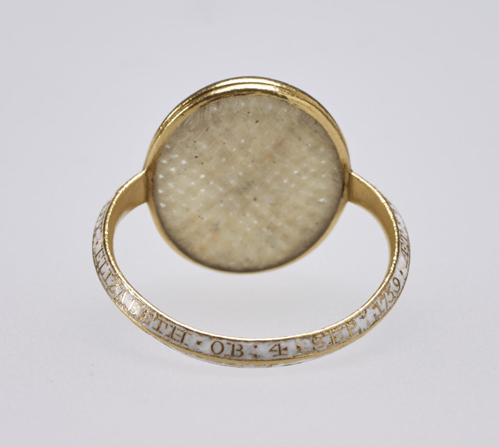 Small gold mourning ring, the centre set with oval crystal containing woven hair and carved with intaglio profile head of Princess Elizabeth, sister of George III, facing right. Inscription on band reads, 'LADY ELIZABETH.OB.FOR.SEP.1759 AET. 18.EN MEMOIRE D'UNE AMITIE CHERE.'