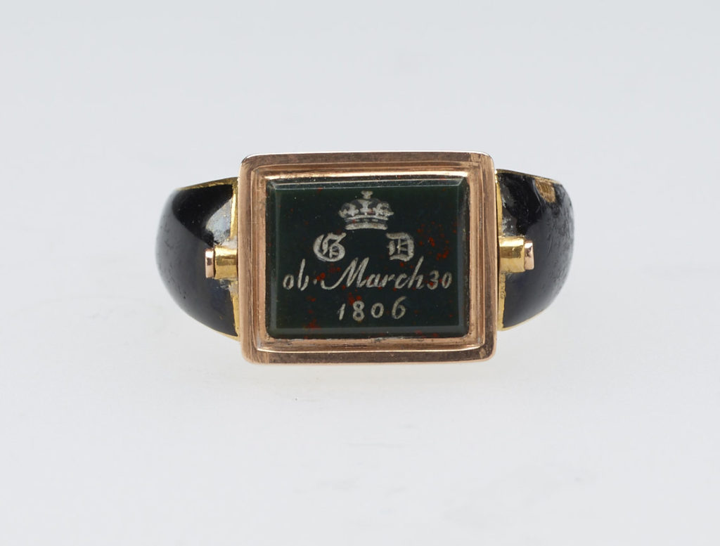 Mourning ring for Georgiana, Duchess of Devonshire (1757-1806). Gold ring, hoop enamelled in black with central hinged rectangular reserve, set with bloodstone carved with ducal coronet above gothic GD monogram and inscription, 'ob. March 30 / 1806'. Back set with woven hair behind glass. 