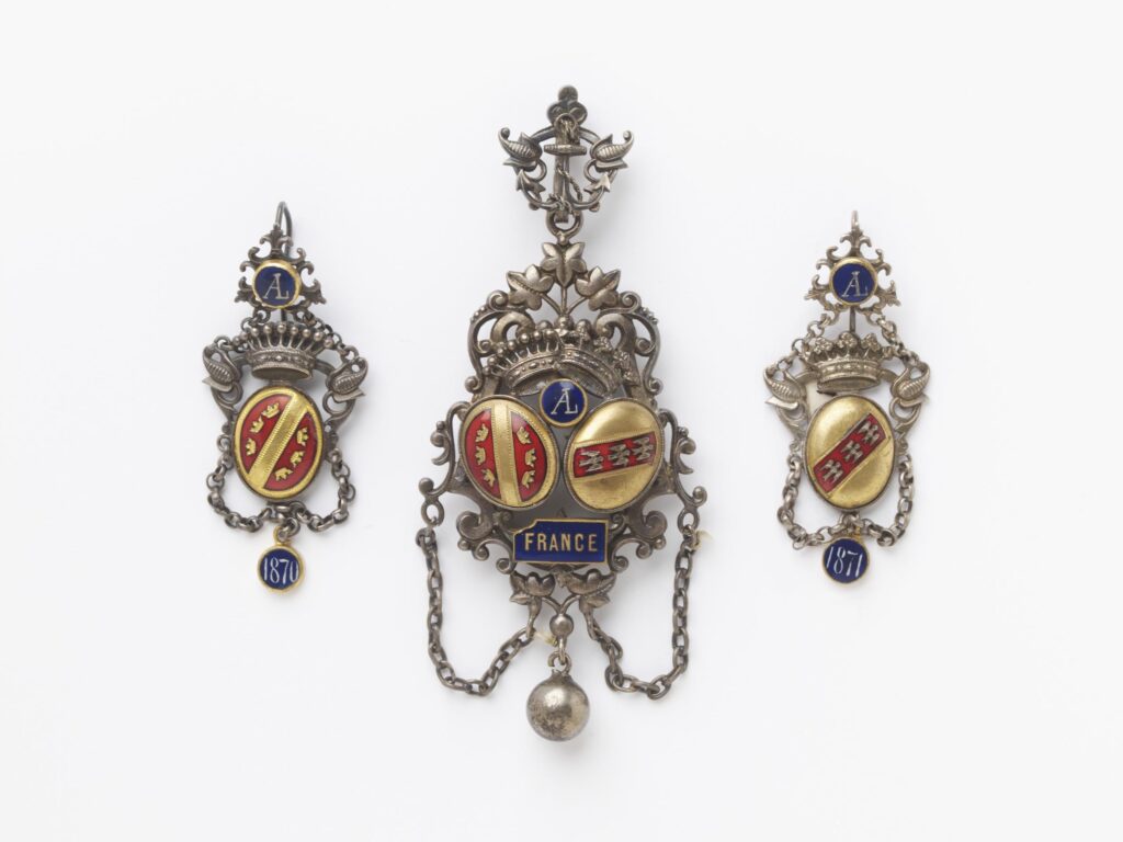 French 1871-1872 souvenir mourning brooch for the loss of Alsace-Lorraine, territories given to the Prussians as war reparations. Oxydised silver-plated metal, with plaques of enamelled gilt metal Courtesy V&A.