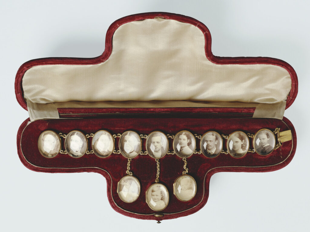 A gilt metal bracelet in the form of 13 sepia portrait photographs set behind convex glass & linked by chains, engraved on back w 'SOUVENIR 1868'; in red velvet & white silk case.